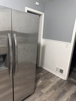 A stainless steel refrigerator in a kitchen with a grey wall and wooden flooring. - 3-bedroom house  2 cozy rooms in peaceful Harvey with shared living space (Harvey)