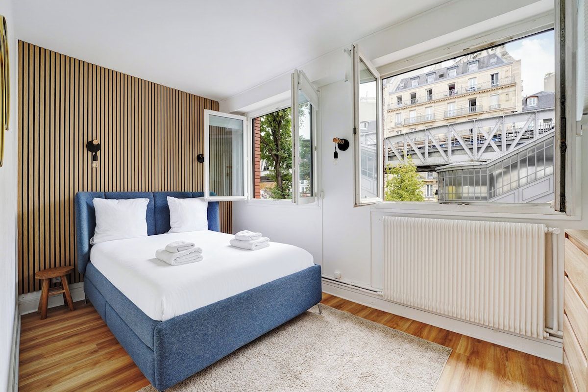 A bedroom with a bed, a window, and a view of buildings.