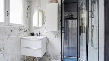 A modern bathroom with a marble wall, a white vanity, a glass shower enclosure, and a large mirror.