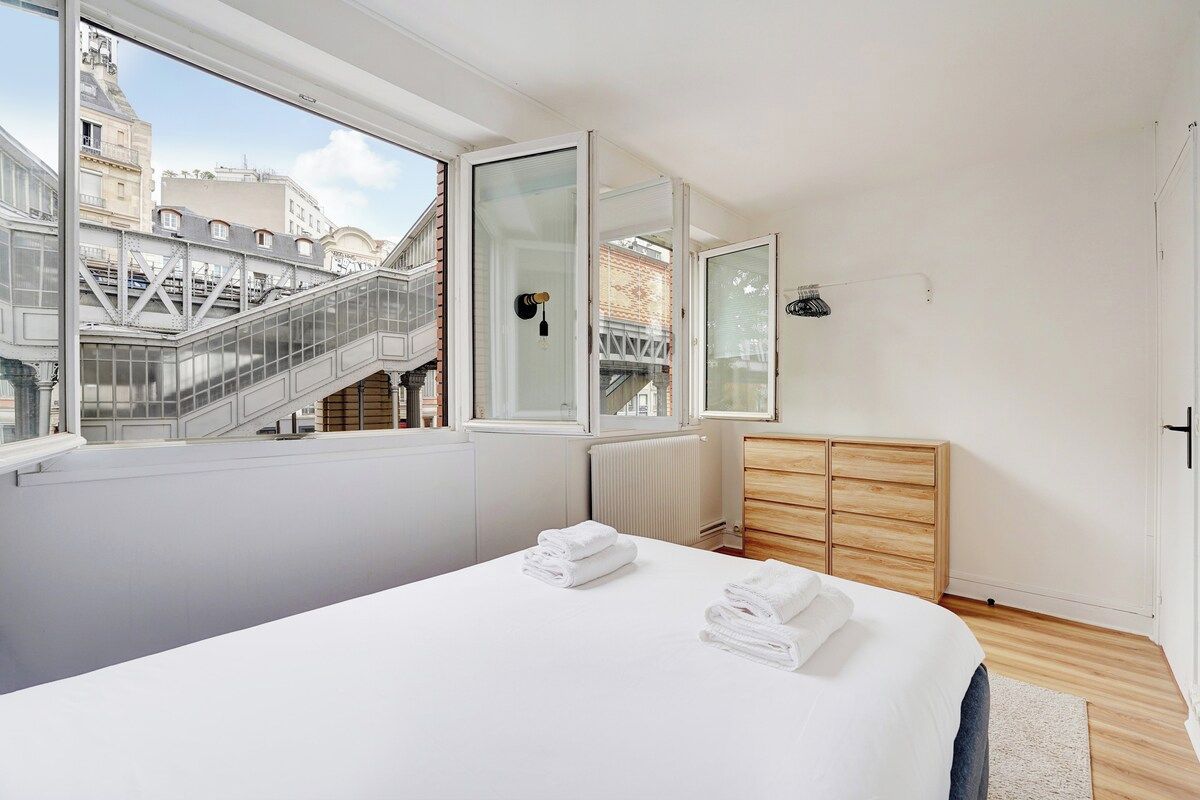 A modern bedroom with a large bed, a wooden wardrobe, and a view of a cityscape through a large window.