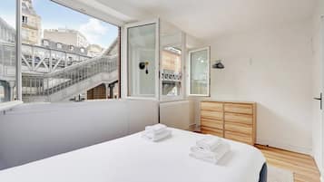 A modern bedroom with a large bed, a wooden wardrobe, and a view of a cityscape through a large window.
