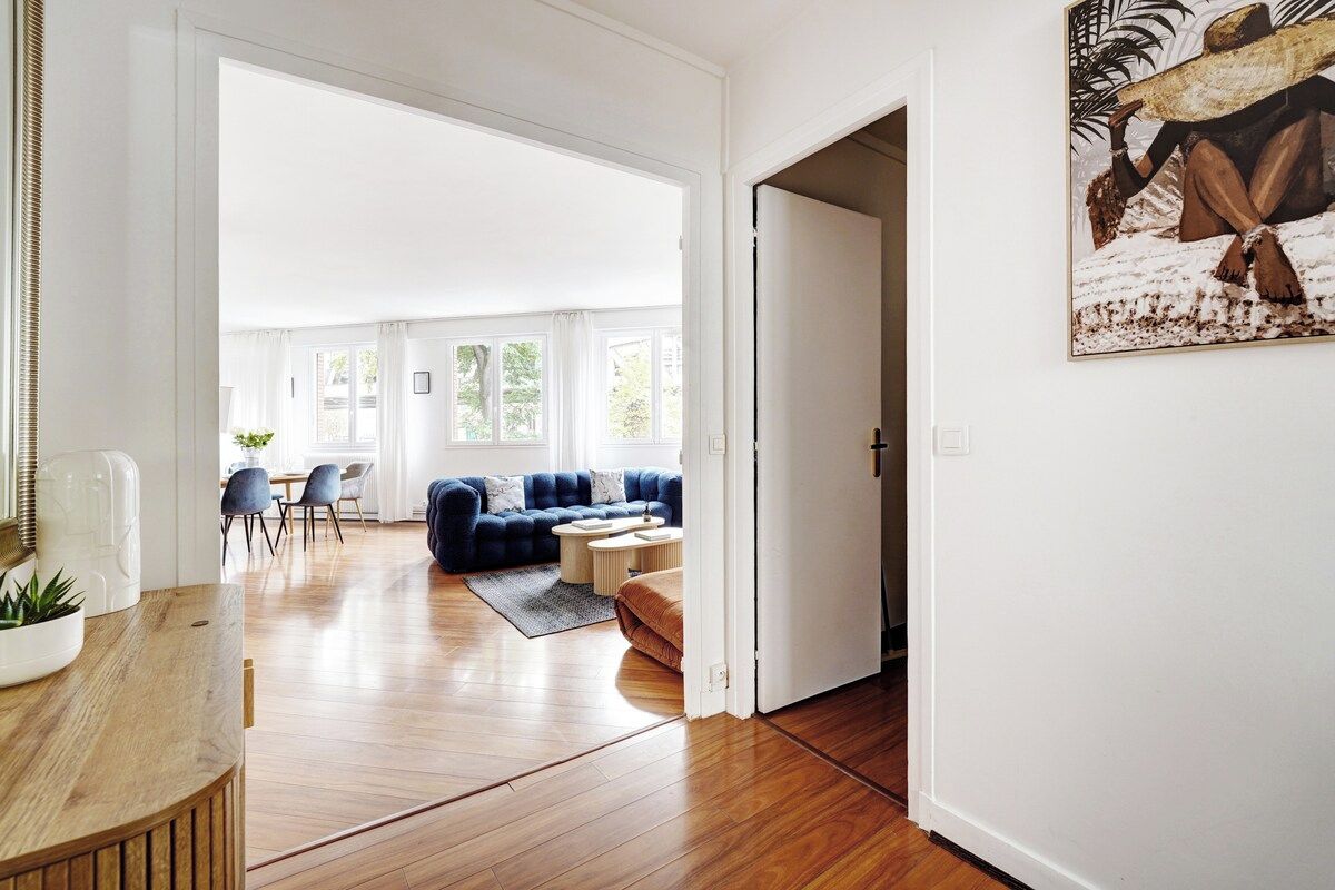 A spacious living area with a blue sofa, wooden flooring, and a dining area with chairs and a table.