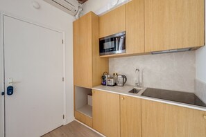 A compact kitchen with wooden cabinets, a microwave, a coffee maker, and a sink. - Incredible Location - Central Studio near Louvre (Paris)