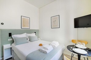 Une chambre d’hôtel avec un lit, une table à manger avec des assiettes et des verres, et des œuvres d’art accrochées aux murs.