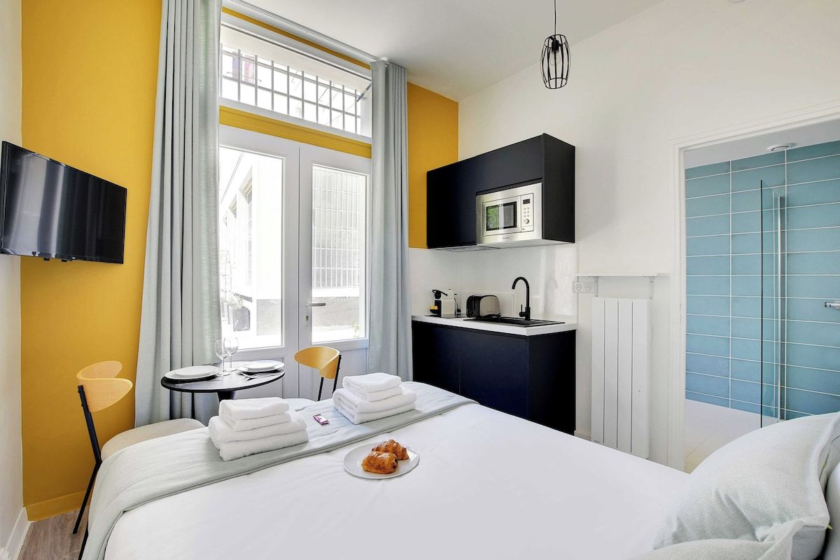 A hotel room with a bed, a small table with a chair, a microwave, and a sink.