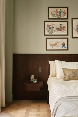 A bedroom with a bed, a nightstand, and three framed artworks on the wall. - Curated Home for an Unforgettable Experience (Paris)