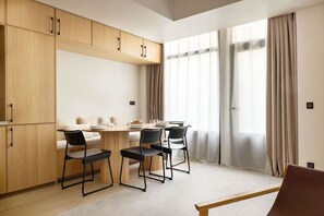 A modern kitchen with wooden cabinets, a dining table with chairs, and large windows with curtains. - Design Flat in Trendy Oberkampf Area (Paris)