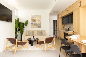A modern kitchen with wooden cabinets, a dining area with a table and chairs, a sofa, and a large plant. - Design Flat in Trendy Oberkampf Area (Paris)