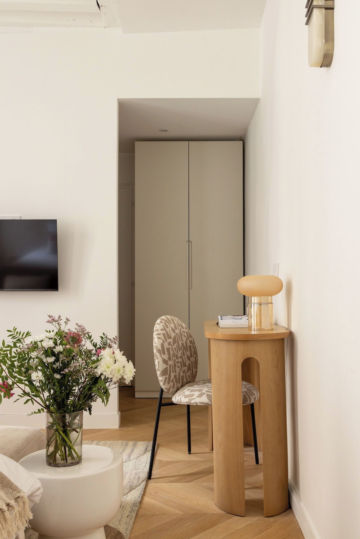 Een moderne woonkamer met een flatscreen televisie, een gestreept fauteuil, een houten bijzettafeltje met een lamp en een bloevas.
