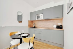 A compact kitchen with grey cabinets, a microwave, a coffee maker, and a dining area with two chairs and a table. - Peaceful Paris Getaway in a Lively Neighborhood (Paris)