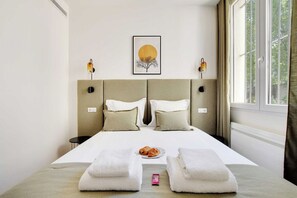 A hotel room with a bed, two bedside lamps, a framed picture on the wall, and a window with curtains. - Peaceful Paris Getaway in a Lively Neighborhood (Paris)