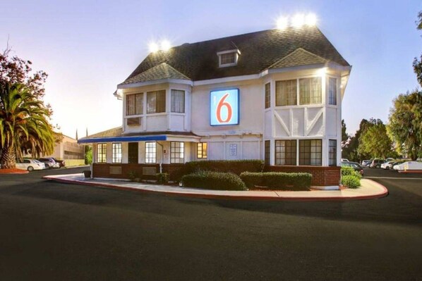 A two-story motel with a prominent '6' sign, a parking lot, and a well-maintained lawn.