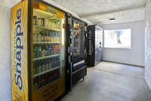 A vending machine with a yellow label and a glass display, located in a hallway with a concrete floor and a window.