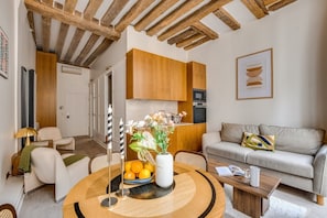 A modern living room with a round coffee table, a sofa, and a dining area with a bowl of fruit. - Chic 1BR only Steps away from the Louvre (Paris)