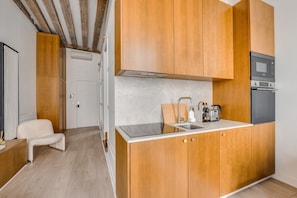 A compact kitchen with wooden cabinets, a built-in oven, and a microwave. - Chic 1BR only Steps away from the Louvre (Paris)
