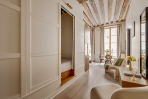 A hotel room with a bed, a desk, and a chair. There is a window with curtains, a wooden floor, and a ceiling with exposed beams. - Chic 1BR only Steps away from the Louvre (Paris)