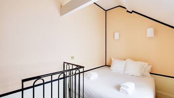 A hotel room with a bed, white linens, a black metal railing, and a small window.