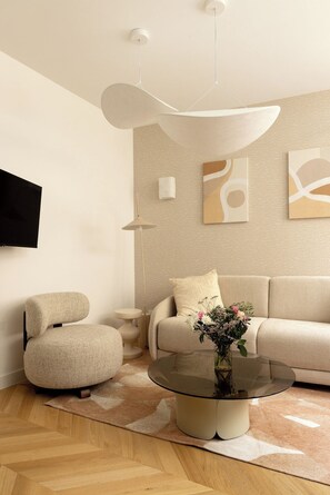 A modern living room with a sofa, armchair, and a glass coffee table with a vase of flowers. - Redesigned Calm Retreat in the Heart of Le Marais (Paris)