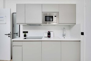 A modern kitchen with a built-in microwave, a sink, and a countertop with a toaster and a bottle of wine. - Cosy Cocoon Nestled in Vibrant 11th - Voltaire (Paris)