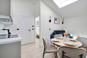 A modern kitchen with a built-in oven and a dining area with a round table and chairs. - Cosy Cocoon Nestled in Vibrant 11th - Voltaire (Paris)