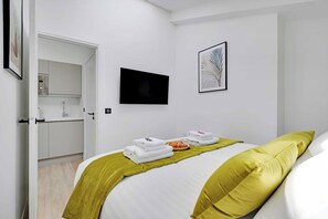 A hotel room with a bed, a television mounted on the wall, a door leading to a bathroom, and a framed artwork on the wall. - Cosy Cocoon Nestled in Vibrant 11th - Voltaire (Paris)