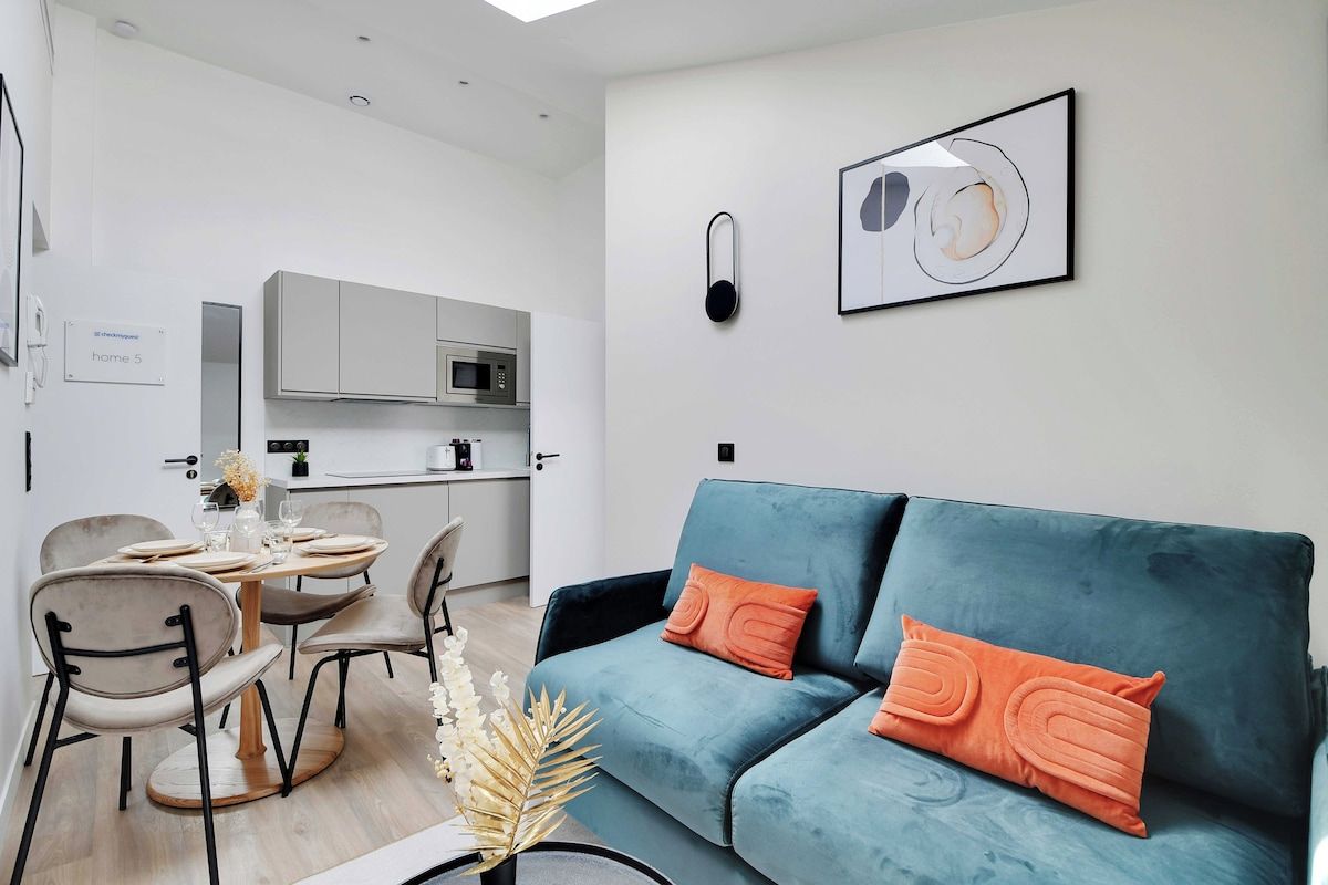 Un salon moderne avec un canapé bleu, une table à manger avec des chaises, et une cuisine en arrière-plan.