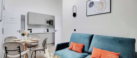 Una sala moderna con un sofá azul, una mesa de comedor con sillas y una cocina al fondo.