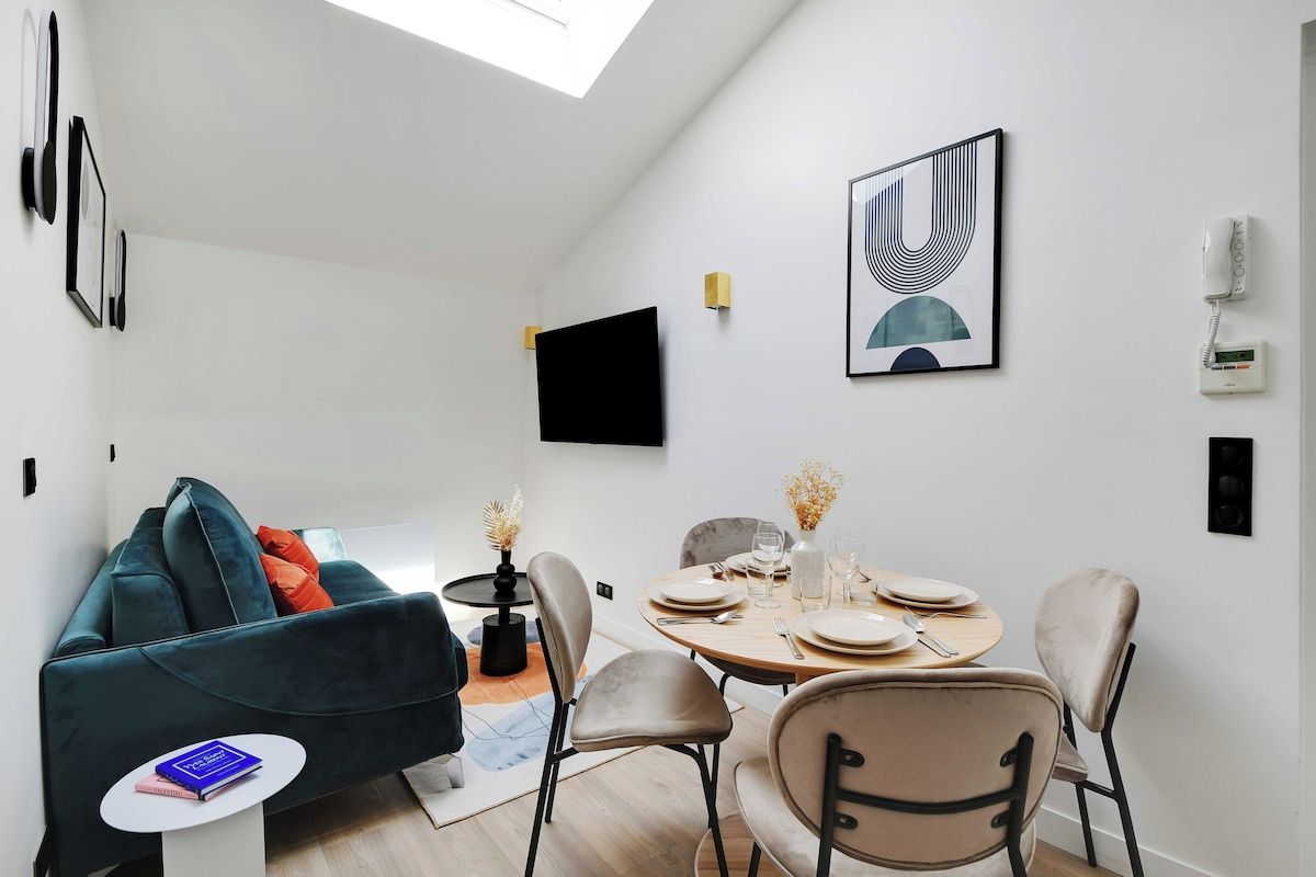 Un salon moderne avec un canapé, une table à manger pour quatre personnes et un téléviseur à écran plat fixé au mur.