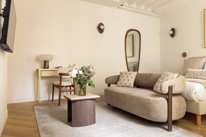 A living room with a sofa, a coffee table, a chair, a small desk, and a mirror. - Brand New Flat in Central Marais - Walk Everywhere (Paris)