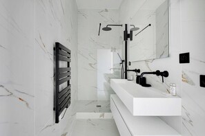 A modern bathroom with a marble wall, a black towel rack, a white vanity, and a shower with a black faucet. - Sleep Above the Parisian Clouds - 1BR - Voltaire (Paris)