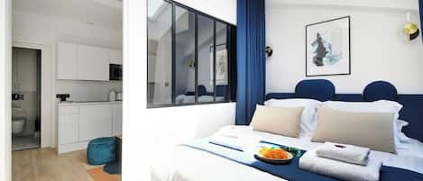 A modern hotel room with a large bed, a dining area, and a view of the city.