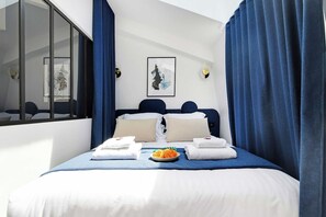A hotel room with a bed, two pillows, a plate of food, and a framed picture on the wall. - Sleep Above the Parisian Clouds - 1BR - Voltaire (Paris)