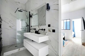 A modern bathroom with a glass-enclosed shower, a white vanity with a mirror, and marble walls. - Sleep Above the Parisian Clouds - 1BR - Voltaire (Paris)