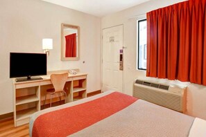 A hotel room with a bed, a desk with a chair, a television, a mirror, a door, and a window with curtains.
