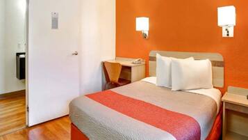 A hotel room with a bed, a desk, a chair, and a nightstand.