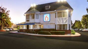 A two-story motel with a prominent '6' sign, a parking lot, and a well-maintained lawn.