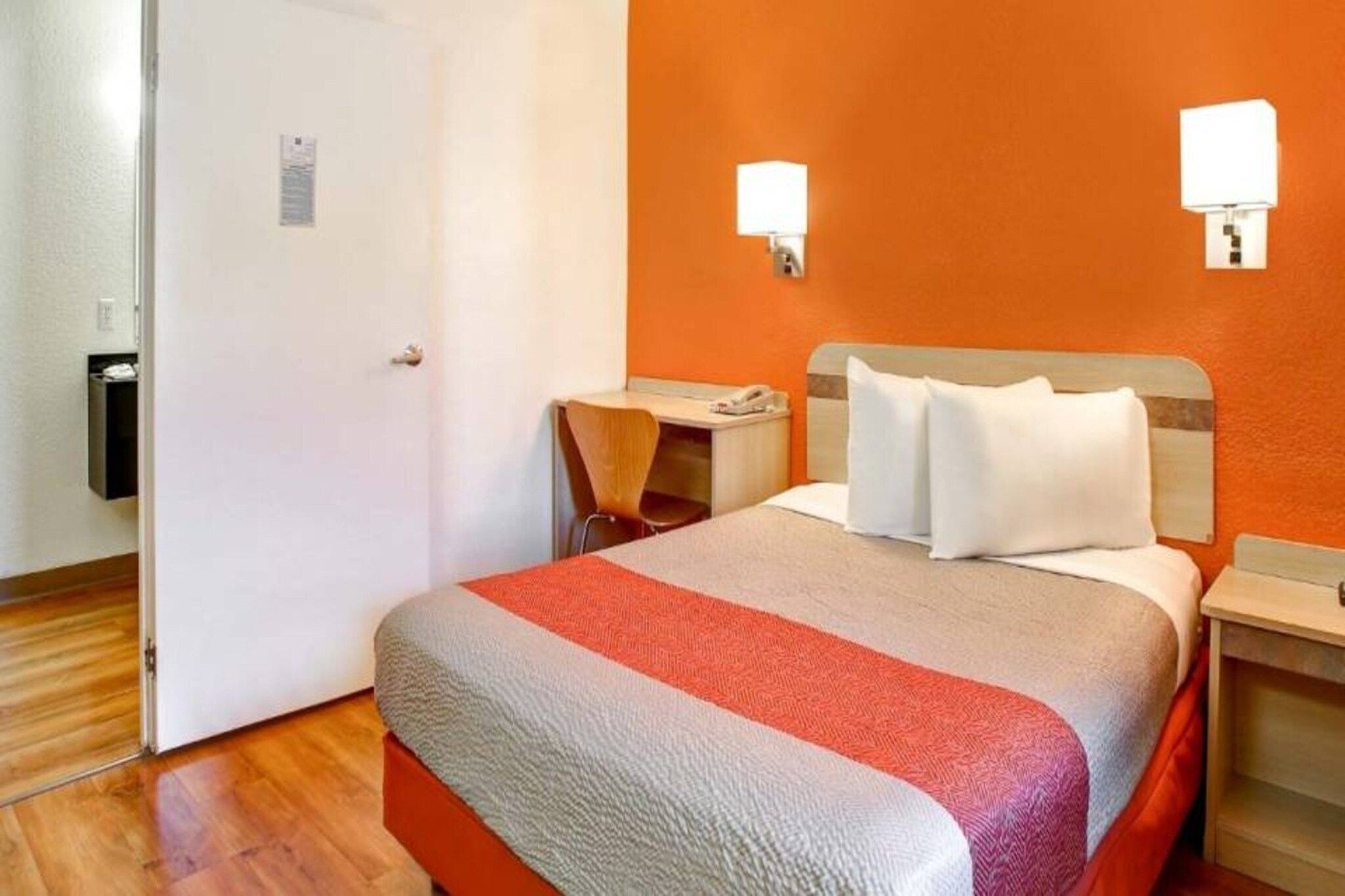 A hotel room with a bed, a desk, a chair, and a nightstand.