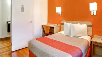 A hotel room with a bed, a desk, a chair, and a nightstand.