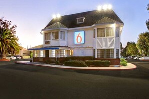 A two-story motel with a prominent '6' sign, a parking lot, and a well-maintained lawn.