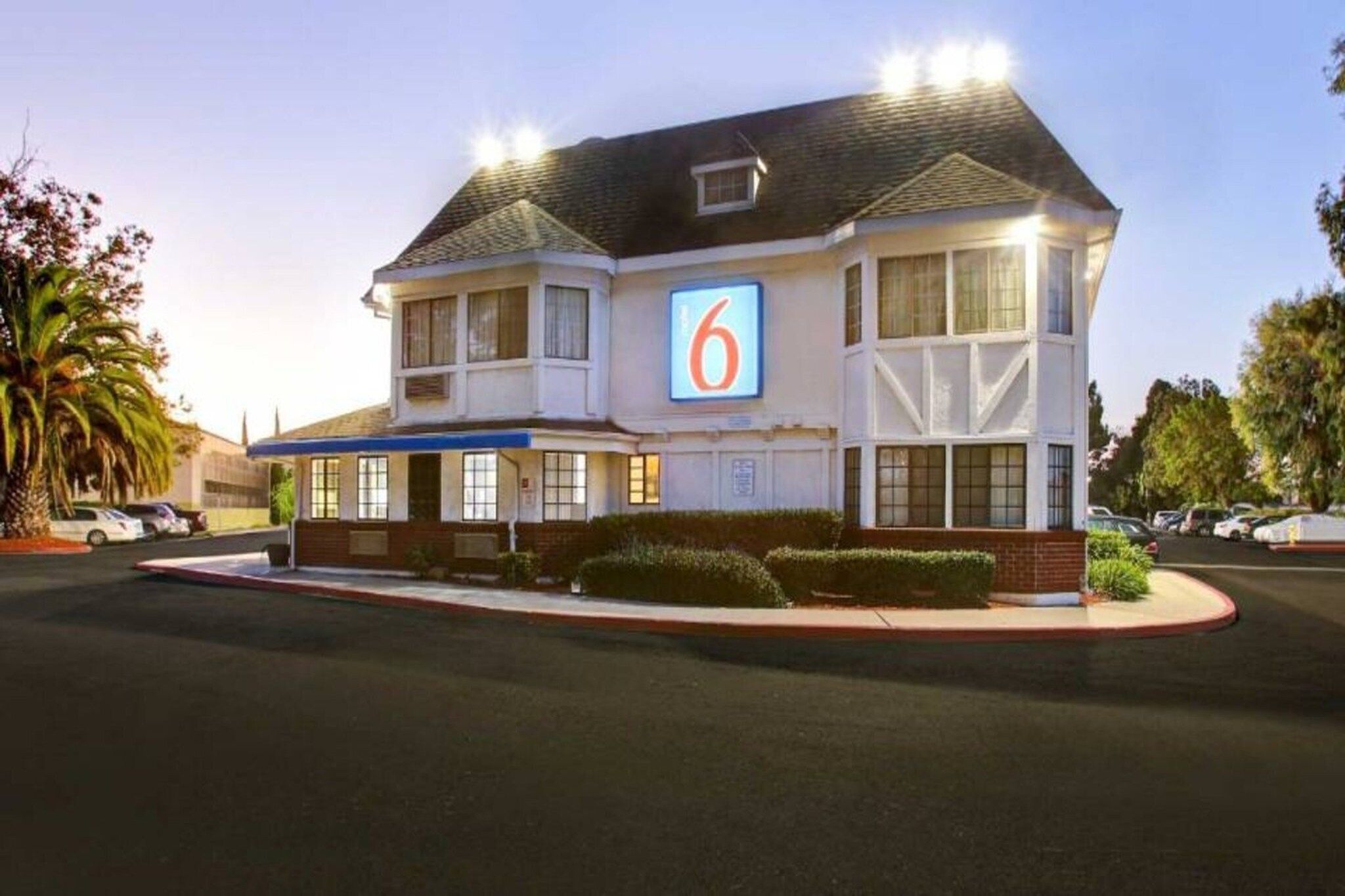 A two-story motel with a prominent '6' sign, a parking lot, and a well-maintained lawn.