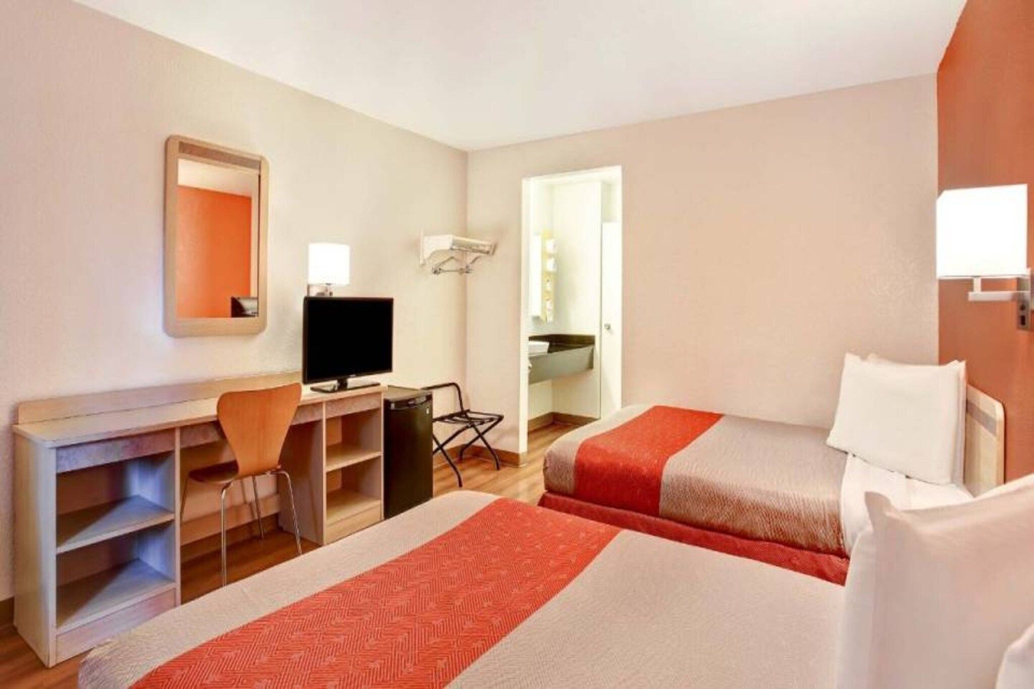 A hotel room with two beds, a desk, a chair, a television, and a mirror.