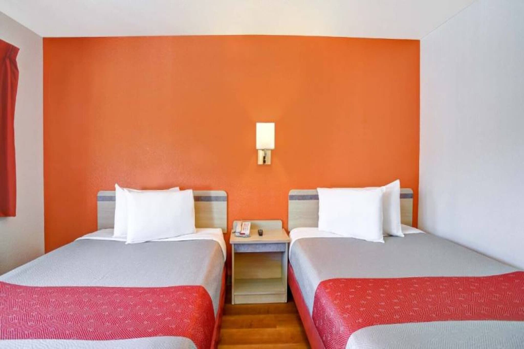 Une chambre d’hôtel avec deux lits, une table de chevet et une lampe fixée au mur.