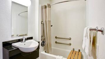 Ein Badezimmer mit einem weißen Waschbecken, einem Spiegel, einer Dusche mit Glastür und einer Badewanne mit hölzernem Sitz.