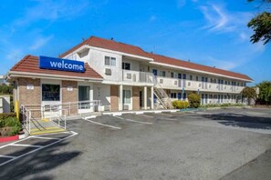 Ein zweistöckiges Motel mit einem 'Welcome'-Schild, einem überdachten Parkbereich und blauem Himmel.