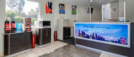 A reception area with a digital screen displaying a cityscape, a counter with a computer, and a window with a view of trees.