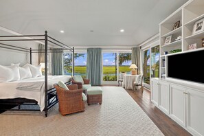 A bedroom with a four-poster bed, wicker furniture, a television, and a view of a green landscape.