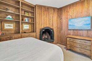 Una habitació amb una llar de foc, prestatges de fusta, un llit i una televisió.