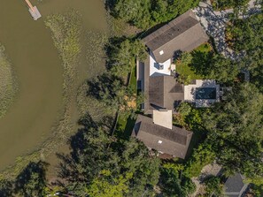 Una casa amb un gran terrat, envoltada d'arbres densos i una massa d'aigua.