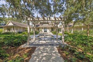 A covered walkway leading to a building with a symmetrical facade, surrounded by lush greenery and a well-maintained garden.