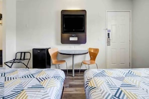 Ein Hotelzimmer mit zwei Betten, einem kleinen Tisch, zwei Stühlen, einem Fernseher und einer Tür.